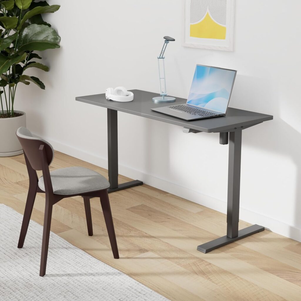 Best Standing Desks for Apartments and Small Rooms (2026) Sansne electric height-adjustable standing desk with black frame and laptop, paired with a wooden chair on hardwood floor.