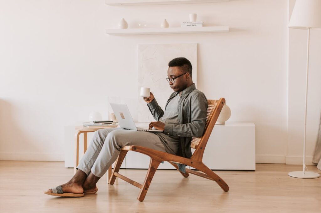 Remote Work Productivity Man working on a laptop from a wooden lounge chair at home, illustrating remote work productivity and flexibility.
